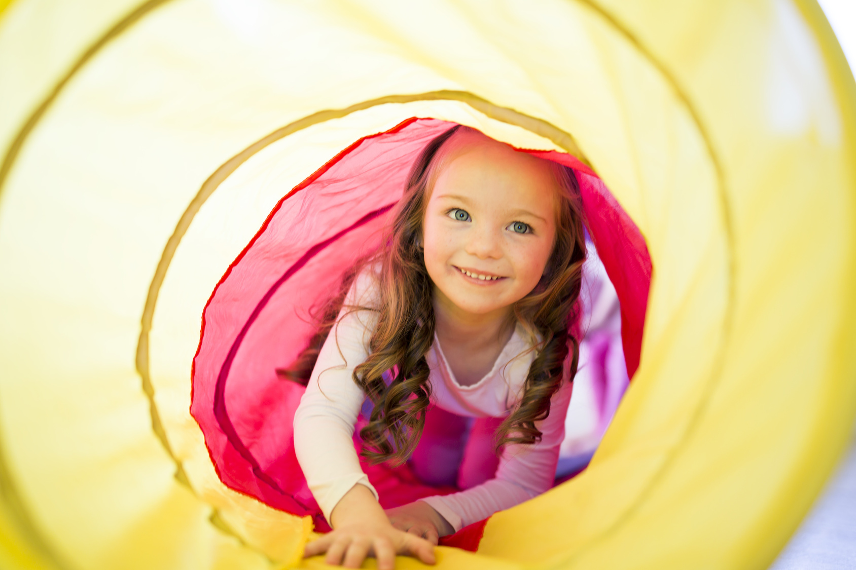 Happy child girl plays indoor in a tunnel