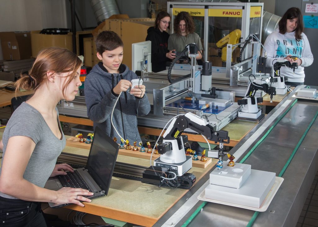 Leona (16) und Luis (14) arbeiten vorne an der Modell-Fertigungsstraße des TGM, einer echten Mini-Fabrik für Industrie 4.0. Hinten kümmern sich Paula, Jakob und Carmen (von links nach rechts), alle 14 Jahre alt, um Einstellungen und Ablauf.