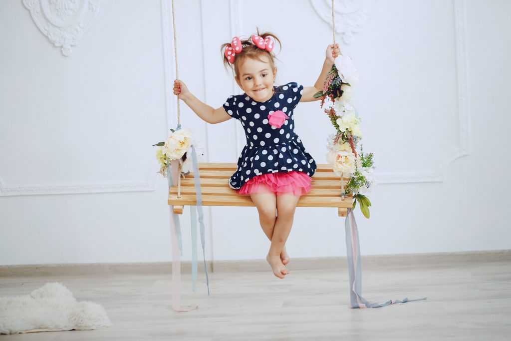 Indoorschaukel cute little girl in a blue dress sitting on the swing at home