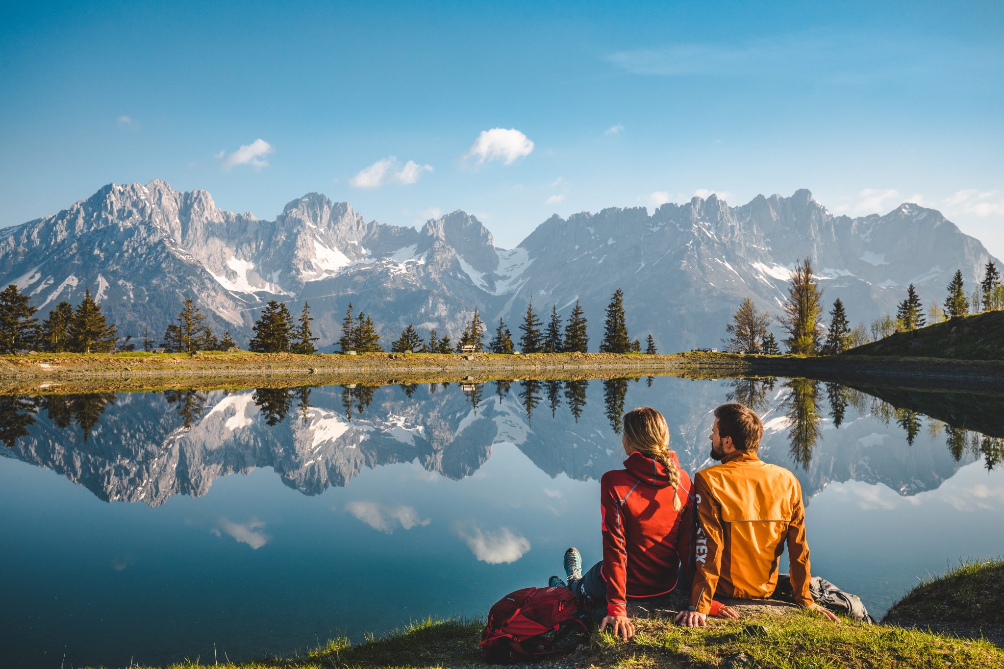 Zwei Menschen sitzen mit Blick auf den Wilden Kaiser am Astbergsee in Going.