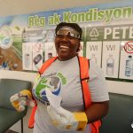 A female in a Social Plastic t-shirt and safety equipment inside a branch. Big smile/laugh.