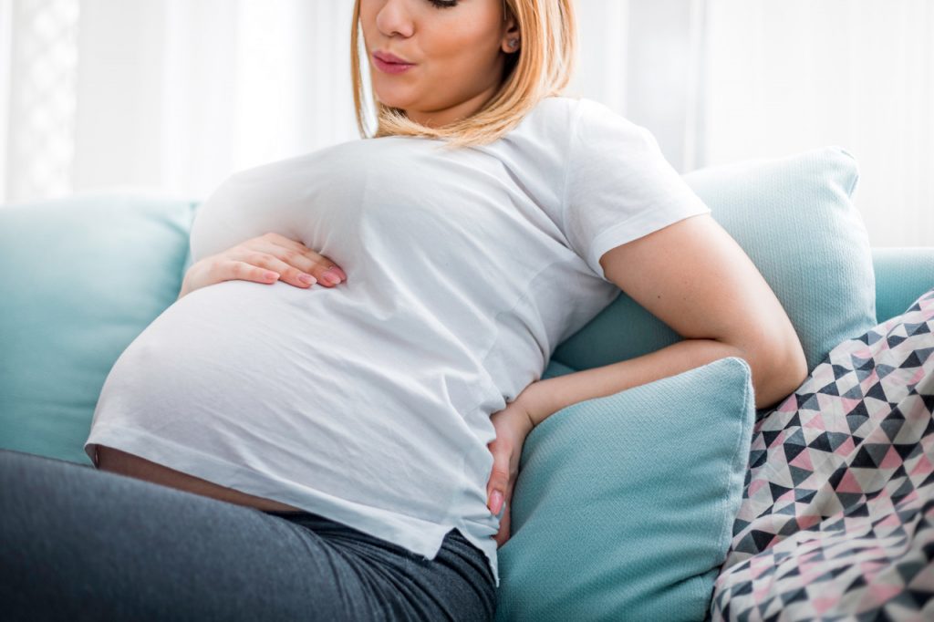 Pregnant woman suffering from backache on sofa at home