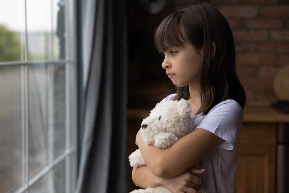 Close,Up,Lonely,Little,Girl,Hugging,Toy,,Looking,Out,Window,