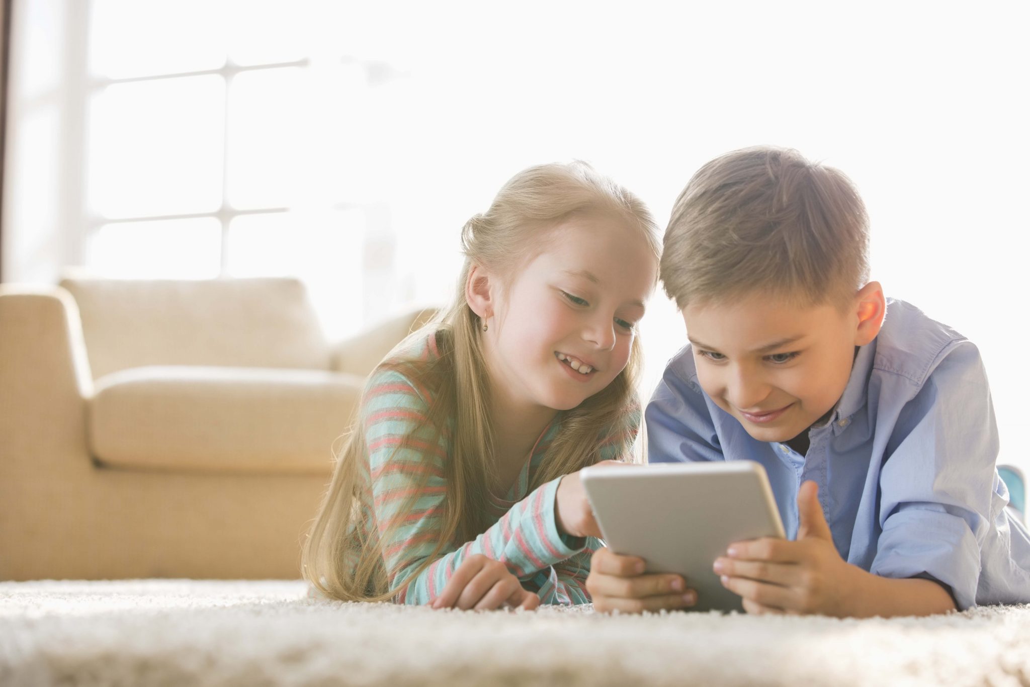 Brother and sister using digital tablet on floor at home