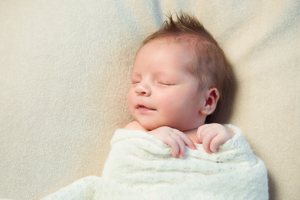 Smiling,Newborn,Baby,With,Mohawk,Hair,Sleeping,In,White,Blanket.