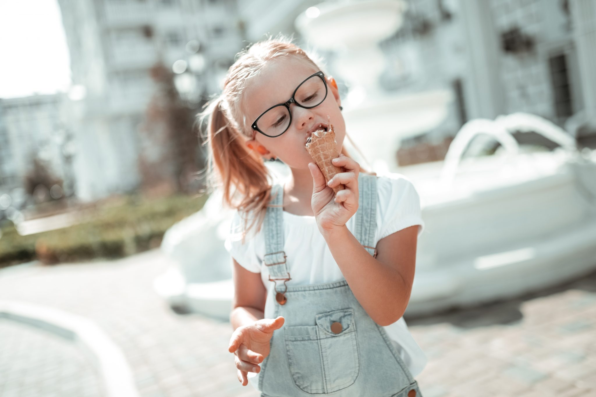 Sweet tooth. Concentrated little girl enjoying her ice-cream cone eating it closing her eyes in the summer.