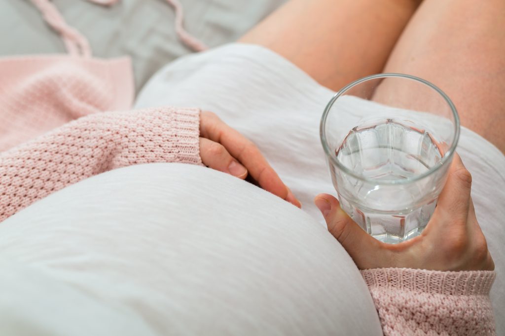 Pregnant woman drinking water. Aerial close up view.