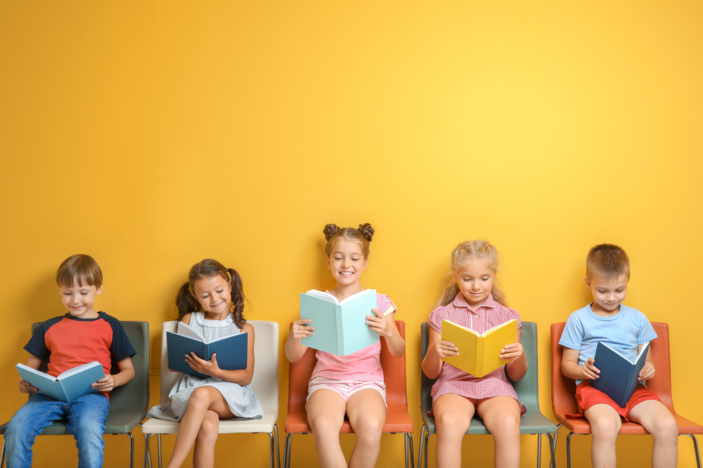 Cute,Little,Children,Reading,Books,While,Sitting,Near,Color,Wall