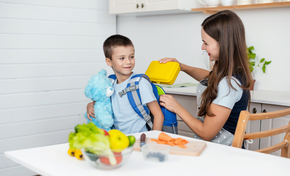 Caring,Mother,Puts,Yellow,Plastic,Lunch,Box,To,Her,Son