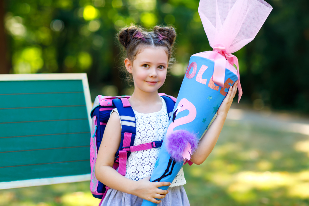 Happy,Little,Kid,Girl,By,Desk,With,Backpack,Or,Satchel
