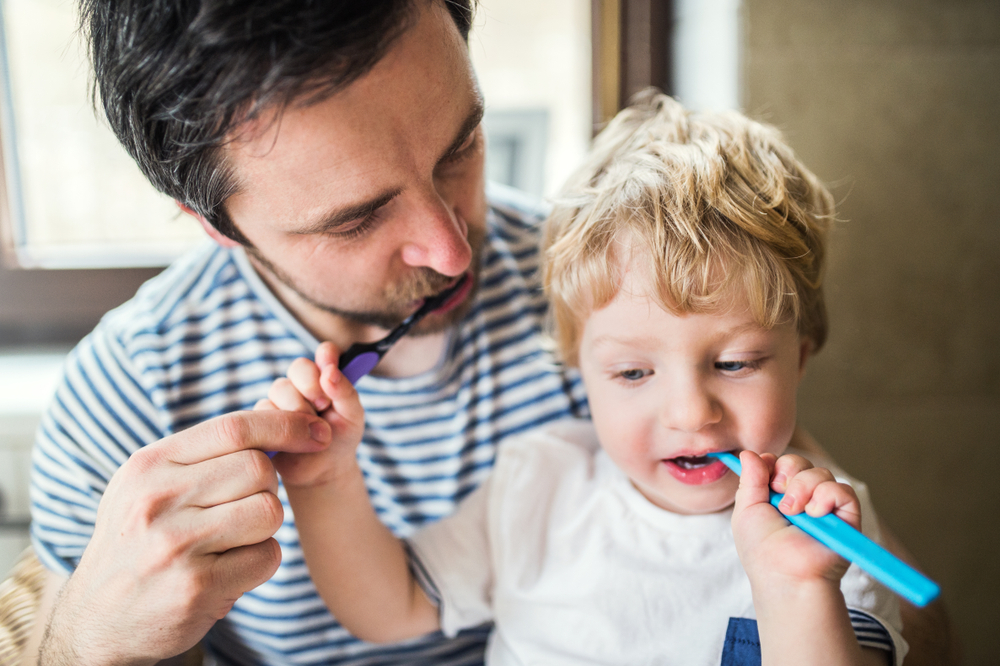 Father,Brushing,His,Teeth,With,A,Toddler,Boy,At,Home.