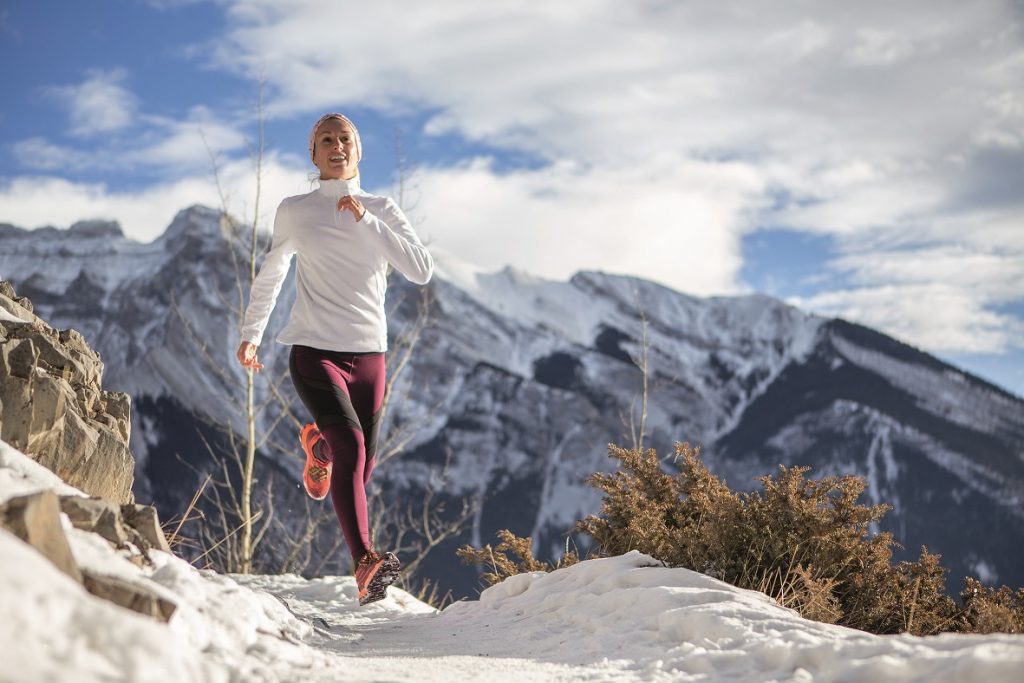 Sportive young woman exercising trail running on mountain trail in Alberta, Canada. People body conscious and heathy lifestyle concept. Winter