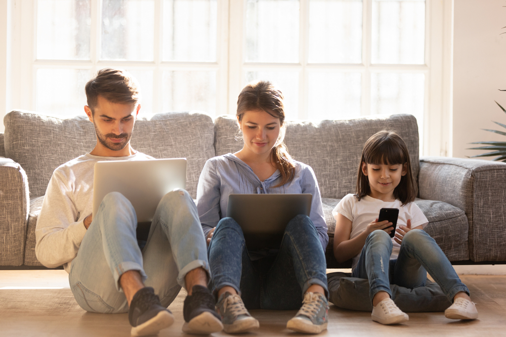 Family,With,Kid,Sitting,On,Floor,At,Home,Using,Laptops
