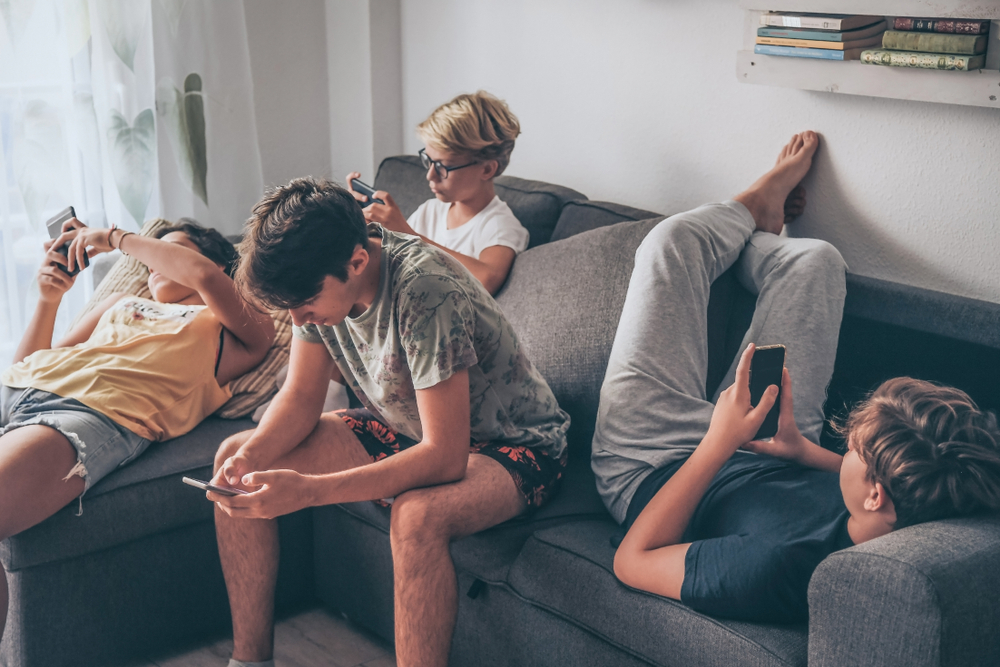 Group,Of,Teenager,Using,Smartphone,Sitting,On,A,Sofa,At
