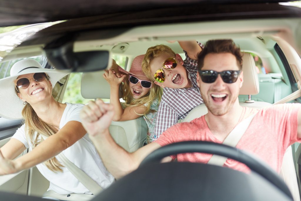 Fröhliche Familie mit Sonnenbrille singt zusammen im Auto auf der Reise